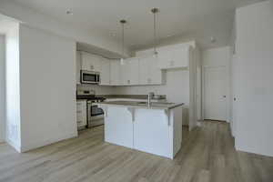 Kitchen featuring white cabinetry, pendant lighting, light hardwood / wood-style floors, an island with sink, and stainless steel appliances