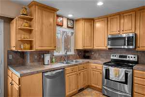 Kitchen featuring appliances with stainless steel finishes, light tile floors, sink, and tasteful backsplash