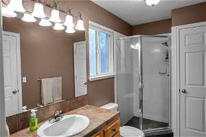 Bathroom featuring vanity with extensive cabinet space, an enclosed shower, a textured ceiling, and toilet
