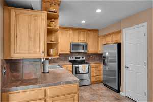 Kitchen featuring tasteful backsplash, light tile flooring, sink, light brown cabinets, and appliances with stainless steel finishes