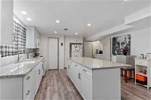 Kitchen with light stone counters, white appliances, white cabinetry, light hardwood / wood-style flooring, and a center island