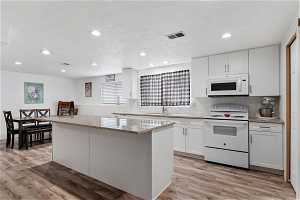 Kitchen with white cabinetry, white appliances, light hardwood / wood-style floors, and a kitchen island