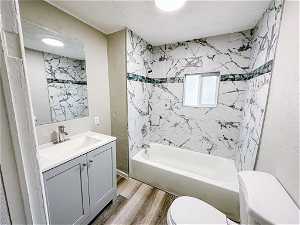 Full bathroom featuring tiled shower / bath, hardwood / wood-style floors, a textured ceiling, toilet, and vanity with extensive cabinet space