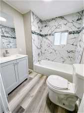 Full bathroom with vanity with extensive cabinet space, hardwood / wood-style flooring, toilet, and tiled shower / bath combo