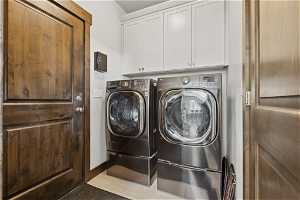 Clothes washing area with light tile floors, washer and dryer, and cabinets