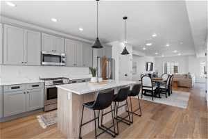 Kitchen featuring light wood-type flooring, a center island, gray cabinets, stainless steel appliances, and light stone countertops
