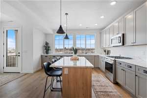 Kitchen with stainless steel appliances, light hardwood / wood-style flooring, a kitchen island, hanging light fixtures, and a kitchen bar