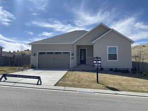 Single story home with concrete driveway, a front lawn, fence, and an attached garage