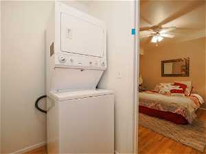 Laundry room with ceiling fan, stacked washing maching and dryer, and light hardwood / wood-style flooring