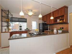 Kitchen featuring tasteful backsplash, ceiling fan, kitchen peninsula, black refrigerator, and stainless steel gas cooktop