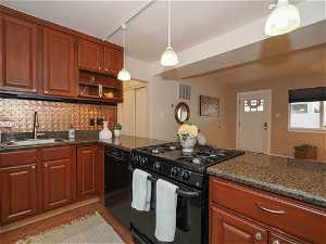 Kitchen featuring light tile flooring, black appliances, sink, backsplash, and hanging light fixtures