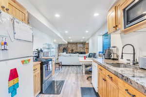 Kitchen with sink, light hardwood / wood-style floors, light brown cabinets, stainless steel appliances, and light stone countertops