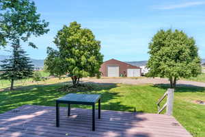 Wooden deck with a garage, a mountain view, a lawn, and an outdoor structure