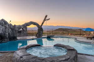 Pool at dusk featuring a mountain view and an in ground hot tub