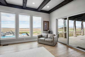 Living room with light hardwood / wood-style flooring, beam ceiling, and a wealth of natural light