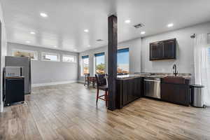 Kitchen with appliances with stainless steel finishes, dark brown cabinets, light stone counters, and a healthy amount of sunlight