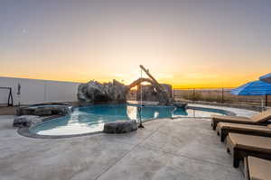 Pool at dusk featuring an in ground hot tub, pool water feature, and a patio