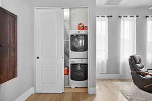 Clothes washing area featuring stacked washing maching and dryer and light hardwood / wood-style floors