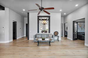 Interior space with ceiling fan with notable chandelier, light hardwood / wood-style flooring, and a towering ceiling