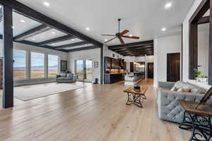 Living room featuring ceiling fan with notable chandelier, light hardwood / wood-style flooring, and beamed ceiling