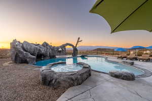 Pool at dusk featuring a patio, a mountain view, and an in ground hot tub