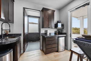 Kitchen featuring sink, dark stone countertops, refrigerator, light hardwood / wood-style floors, and dark brown cabinetry