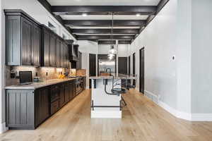 Kitchen featuring a kitchen island with sink, pendant lighting, high quality appliances, a kitchen bar, and light stone counters