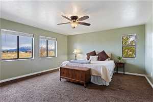 Carpeted bedroom featuring multiple windows, ceiling fan, and a mountain view