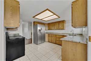 Kitchen featuring sink, stainless range with electric stovetop, light tile floors, stainless steel refrigerator with ice dispenser, and light granite countertops