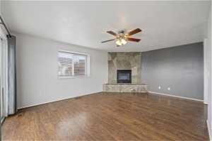 Unfurnished living room with a fireplace, a textured ceiling, dark wood-type flooring, and ceiling fan