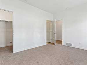 Unfurnished bedroom featuring a spacious closet, light carpet, and a closet