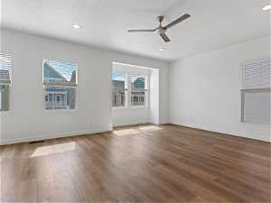 Empty room featuring a healthy amount of sunlight, ceiling fan, a textured ceiling, and hardwood / wood-style floors