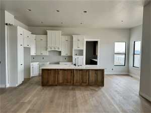 Kitchen featuring white cabinetry, sink, light wood-type flooring, and a kitchen island with sink