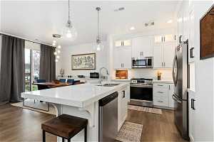 Kitchen with dark hardwood / wood-style floors, appliances with stainless steel finishes, an island with sink, and sink