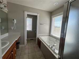 Bathroom featuring vanity with extensive cabinet space, tile floors, a textured ceiling, and a relaxing tiled bath