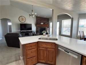Kitchen featuring light colored carpet, stainless steel dishwasher, a fireplace, sink, and lofted ceiling