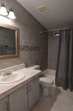 Full bathroom featuring tile walls, shower / tub combo with curtain, tile floors, vanity, and toilet