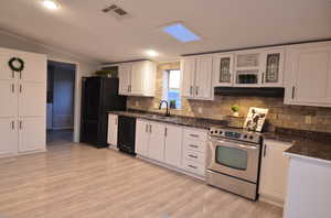 Kitchen with black appliances, sink, laminate flooring, a skylight, and white cabinetry