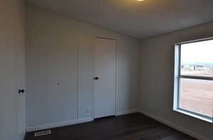 Unfurnished bedroom featuring a textured ceiling, lofted ceiling, a closet, and dark wood-type flooring