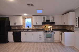 Kitchen featuring black appliances, sink, laminate flooring, and white cabinetry