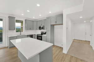 Kitchen featuring a kitchen island, sink, appliances with stainless steel finishes, gray cabinetry, and light hardwood / wood-style floors