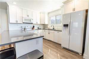 Kitchen with kitchen peninsula, white cabinetry, white appliances, and light hardwood / wood-style flooring