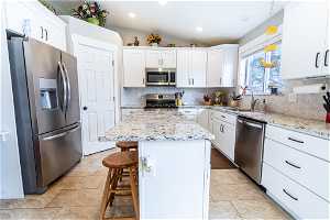 Kitchen with backsplash, white cabinets, stainless steel appliances, a kitchen island, and pendant lighting