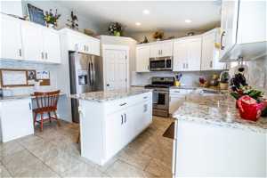 Kitchen featuring light tile flooring, sink, white cabinets, stainless steel appliances, and light stone countertops