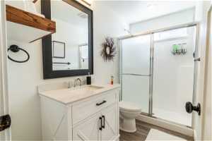 3/4 Bathroom with wood-type flooring, vanity with extensive cabinet space, toilet, and a shower with shower door