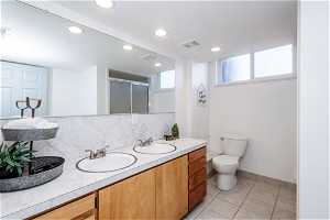 Downstairs bathroom with tile flooring, tasteful backsplash, double vanity, and toilet
