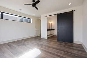 Unfurnished bedroom with dark hardwood / wood-style flooring, a barn door, ensuite bathroom, and ceiling fan