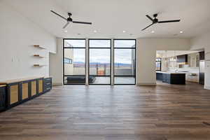 Unfurnished living room featuring dark hardwood / wood-style floors, ceiling fan with notable chandelier, and a wall of windows