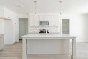 Kitchen featuring white cabinets, decorative light fixtures, appliances with stainless steel finishes, and light wood-type flooring