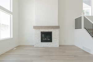 Unfurnished living room featuring a stone fireplace, a towering ceiling, and light wood-type flooring